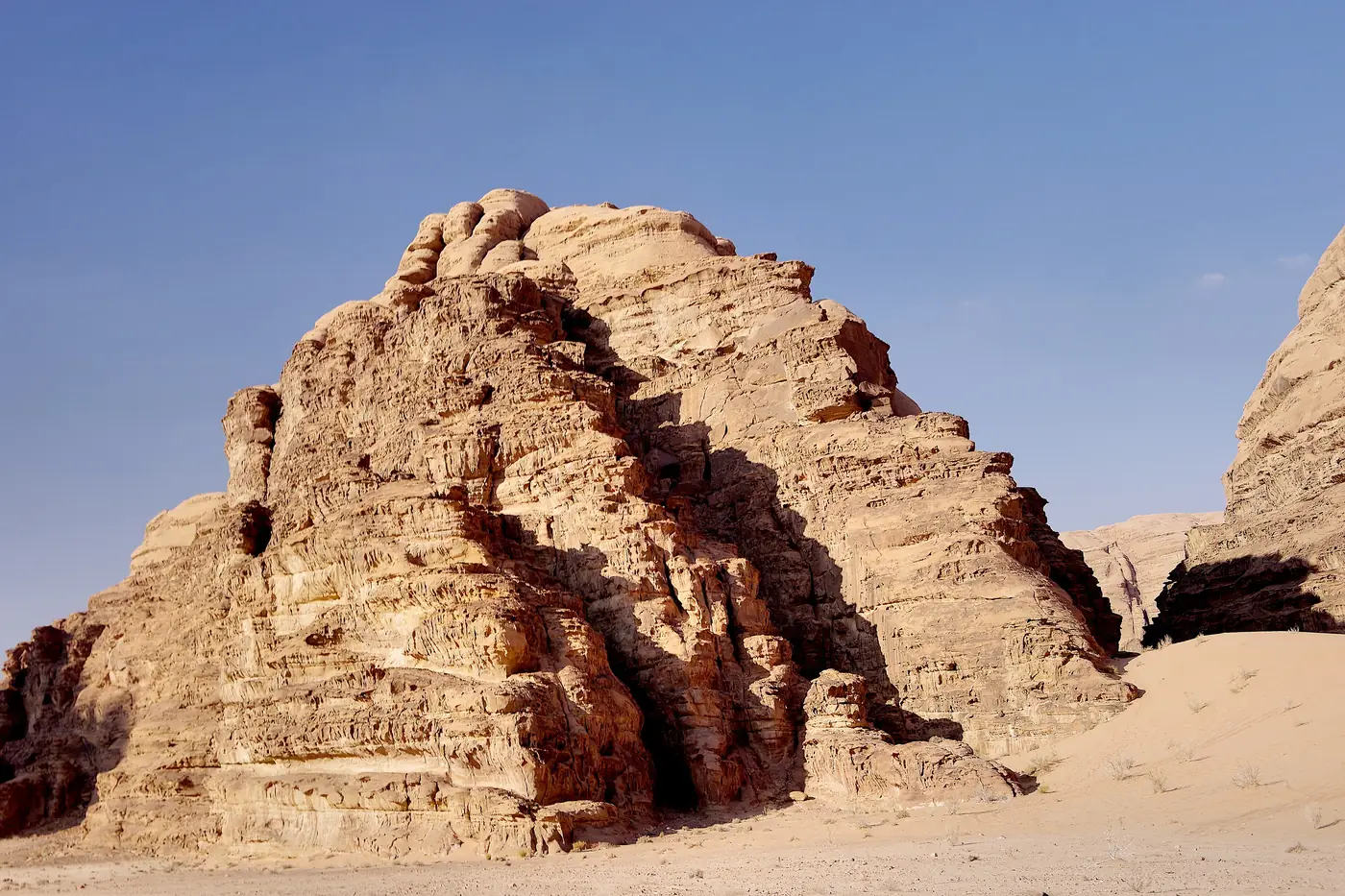 A massive rock formation rising from the sand of Wadi Rum